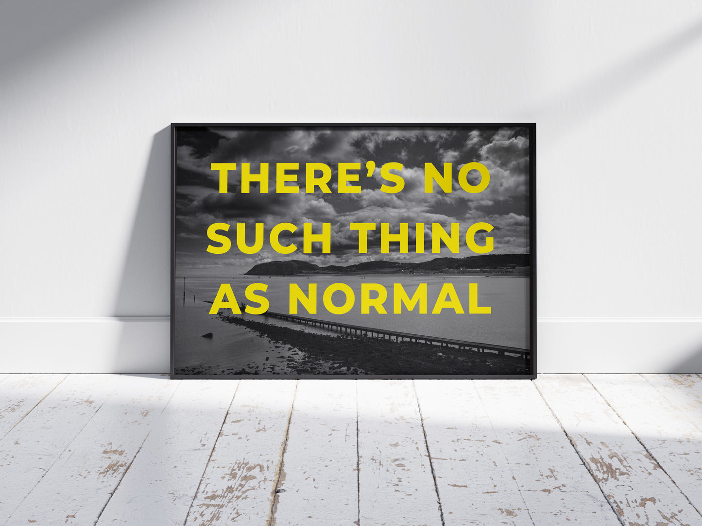 The No Such Thing As Normal art print features bold yellow text in a monochrome design, framed and displayed against a white wall on a light wooden floor.