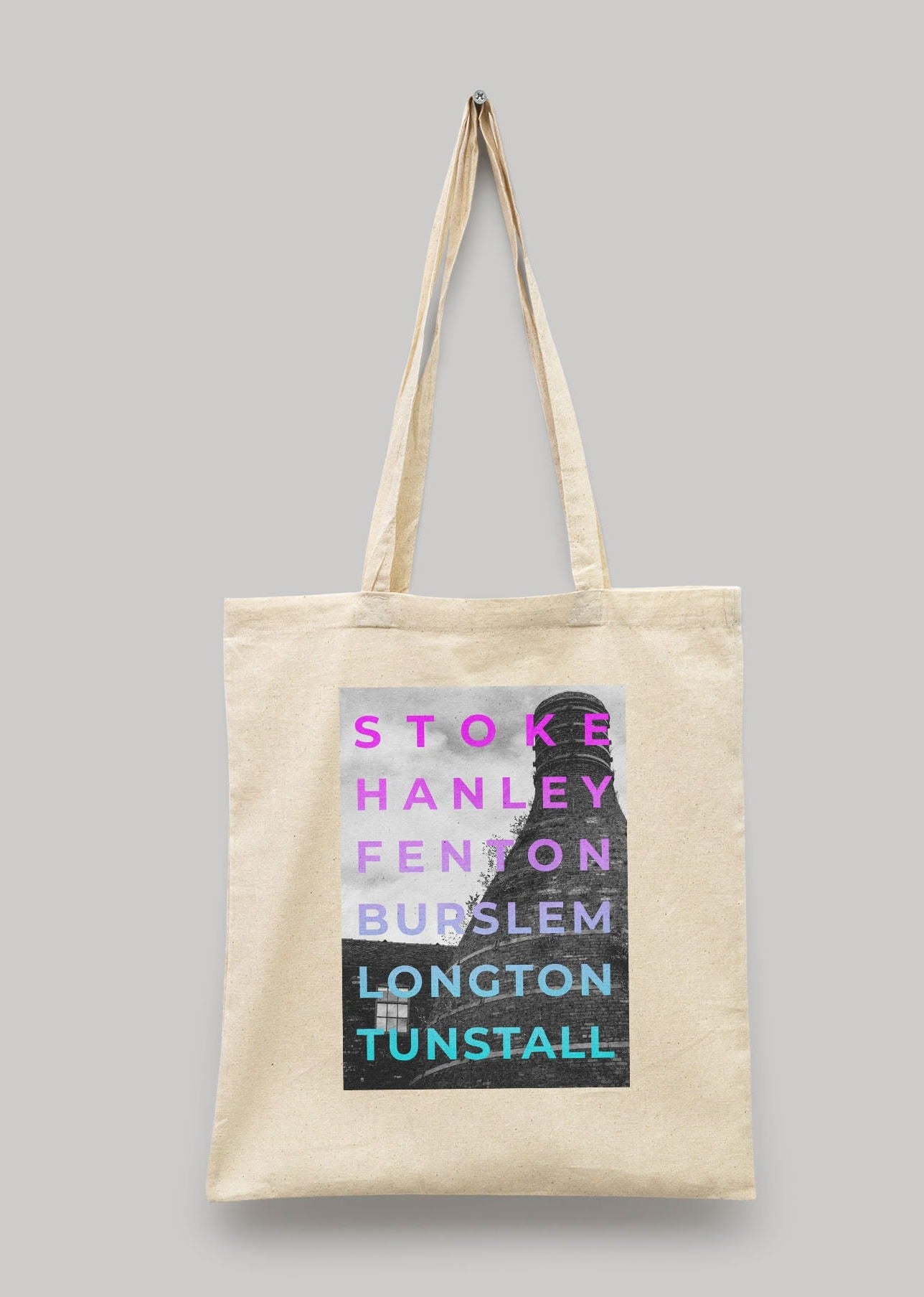 The 6 Towns - Tote Bag is a beige natural cotton canvas tote with long handles, showcasing bold, colorful names of POTTERIES towns over a partial monochrome cityscape graphic.