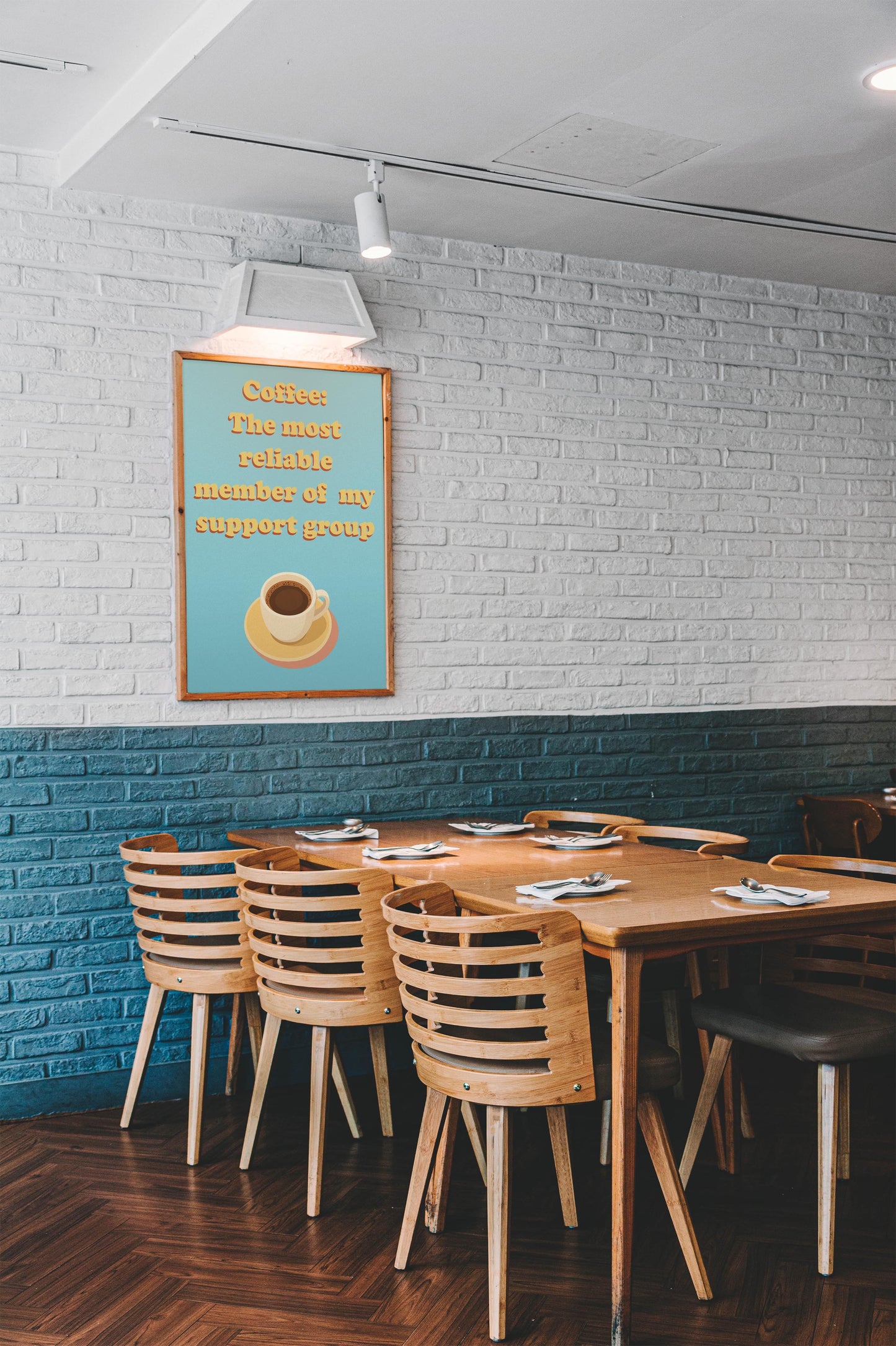 A modern café with wooden tables, stylish decor, white and teal walls, and a Coffee: The Most Reliable Member Of My Support Group - Art Print featuring a coffee cup illustration.