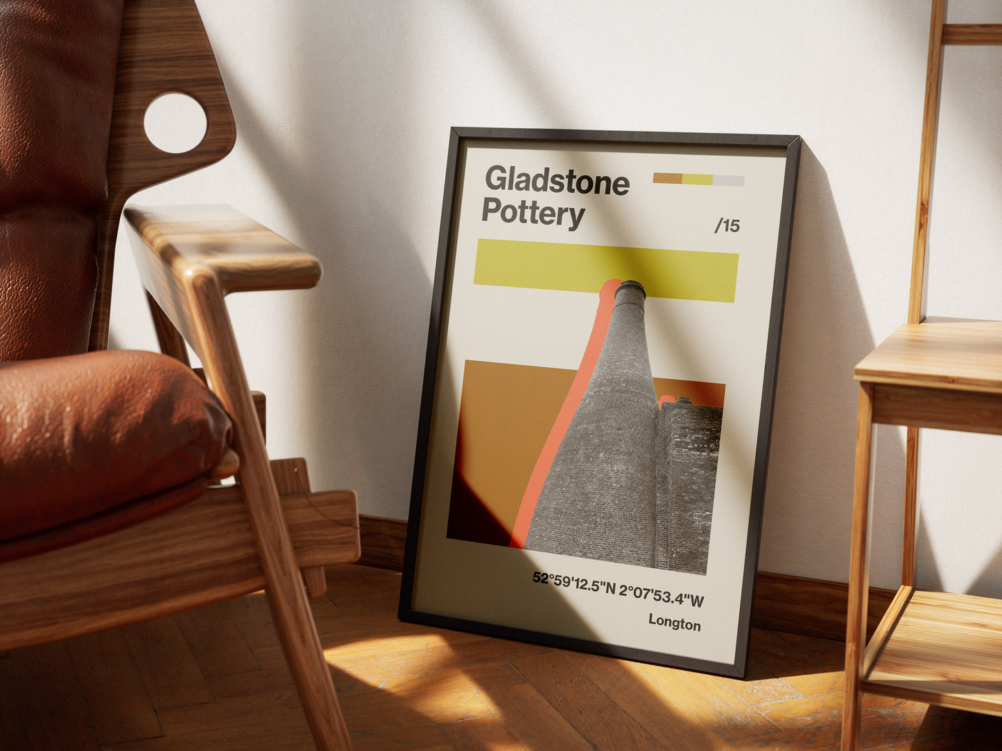 The Gladstone Pottery Poster Print, featuring abstract pottery chimneys, color bars, and coordinates, is framed and leans against a wall on a wooden floor between a chair and small table in Stoke On Trent.
