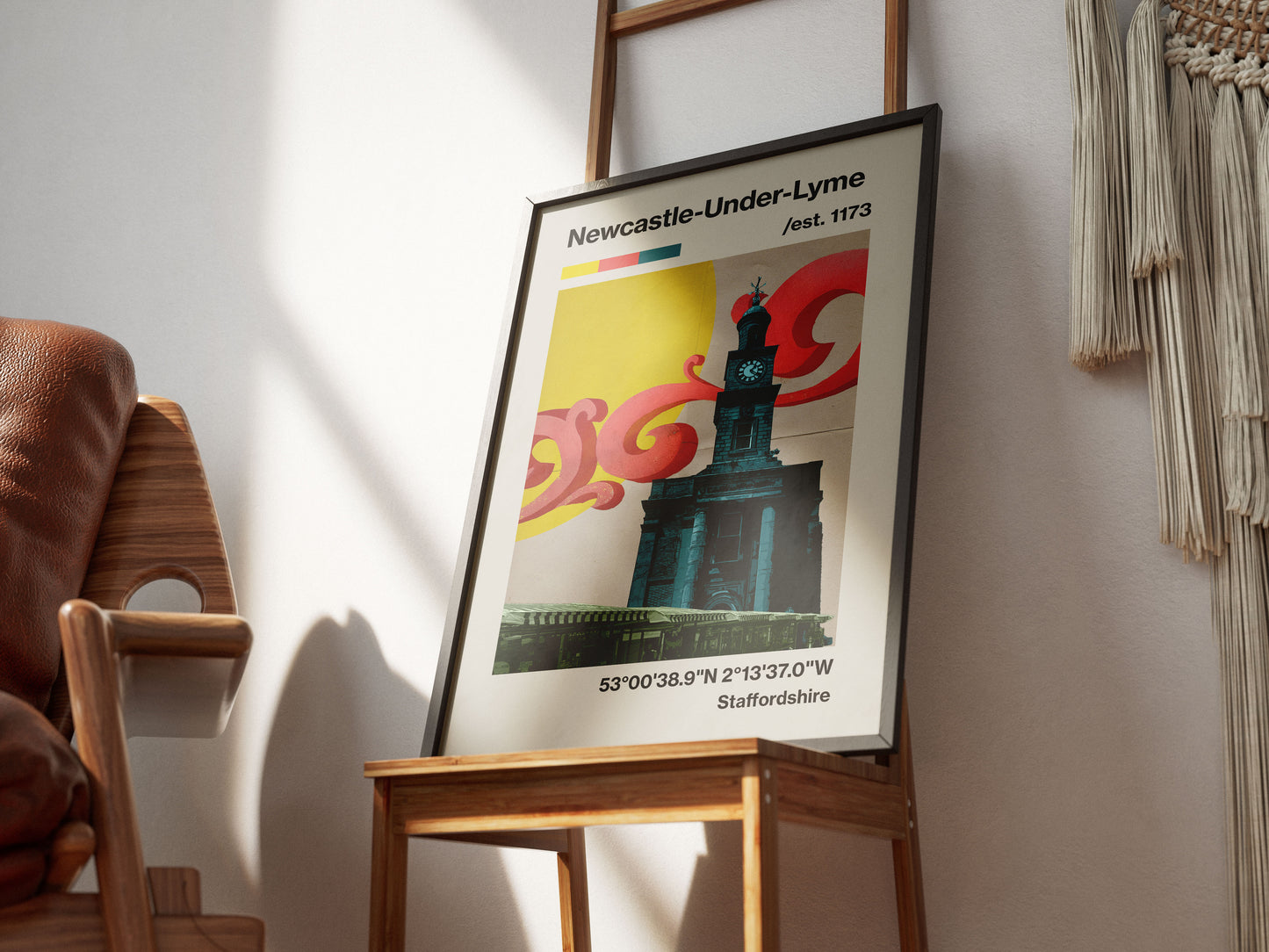 A framed Newcastle-Under-Lyme print rests on a wooden chair, displaying a stylized clock tower, vivid swirls, and coordinates—a tribute to this lively Staffordshire town. Sunlight adds warmth to the inviting room.